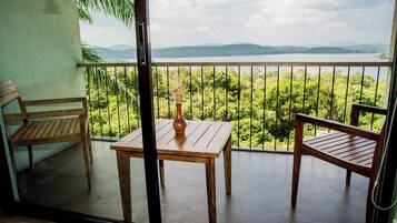 Un balcón con una mesa y sillas de madera, un jarrón y vistas a un lago y montañas.