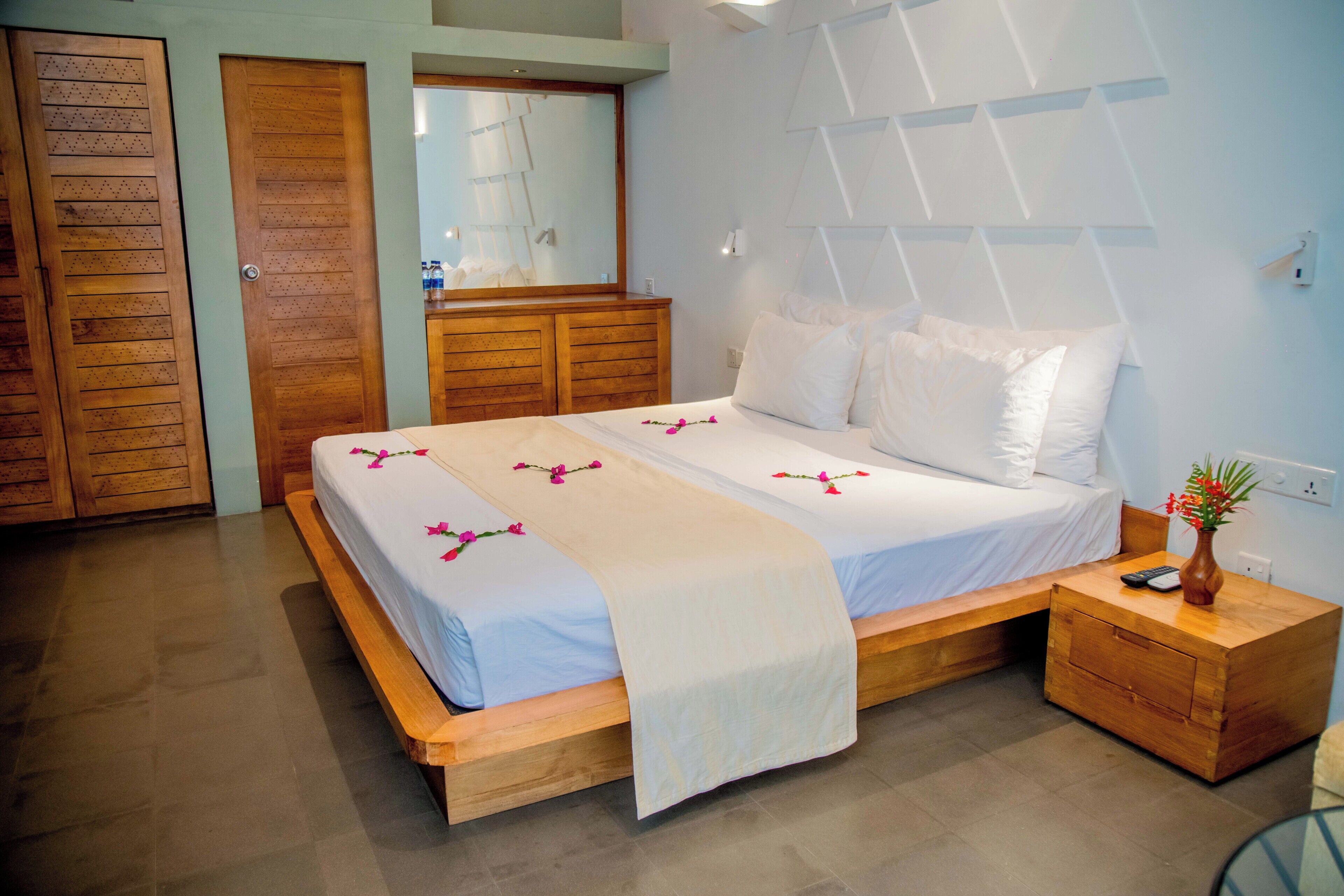 A hotel room with a wooden bed, a nightstand, a mirror, and a wooden wardrobe.