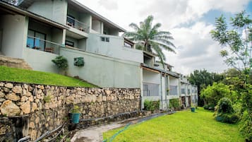 Um edifício com vários andares, um muro de pedra, um gramado e uma palmeira.
