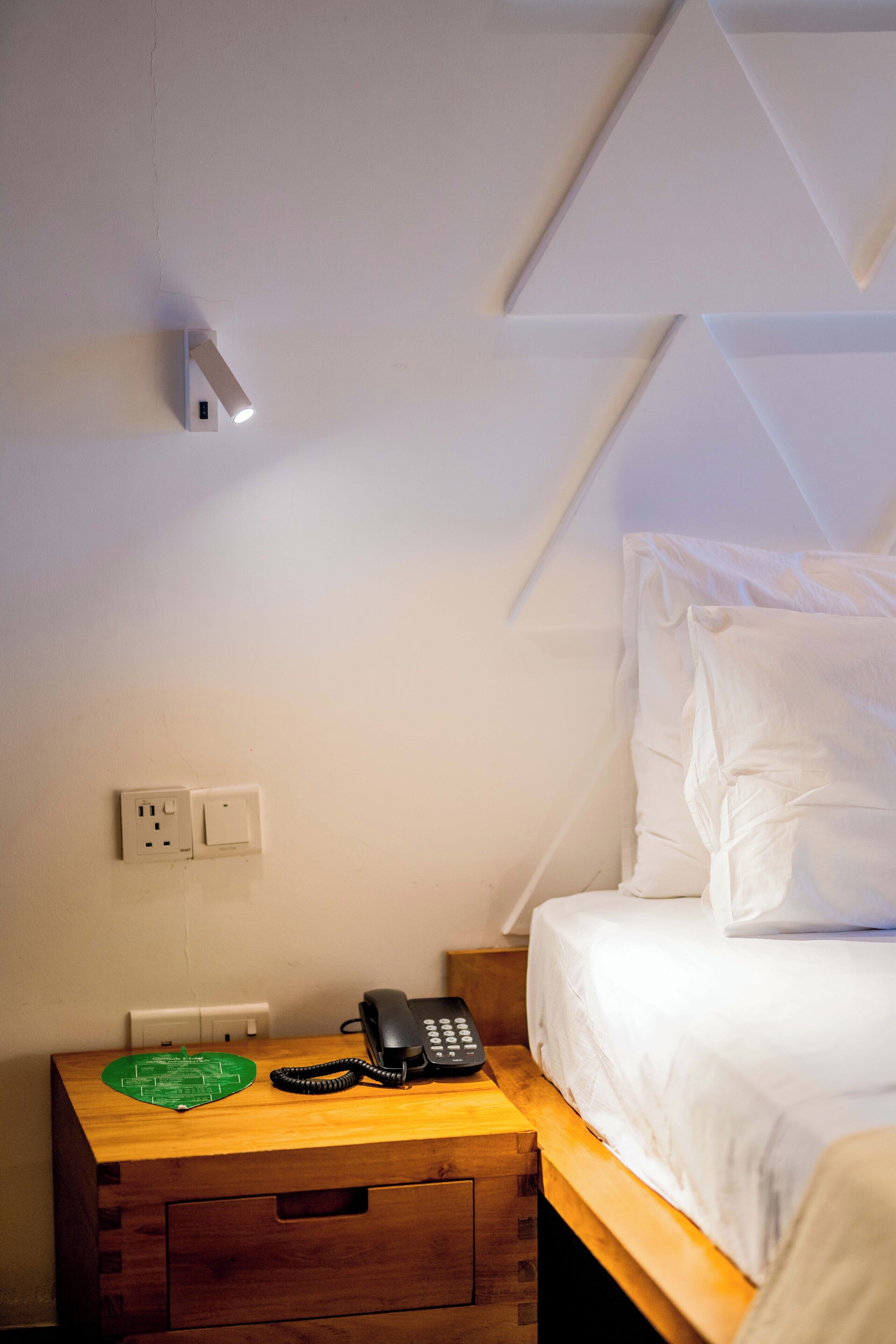A hotel room with a bed, a bedside table with a telephone, and a wall socket.