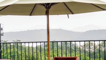 Two lounge chairs with a large umbrella, a railing, and a view of a mountainous landscape.
