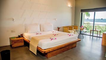 A bedroom with a large bed, wooden headboard, bedside tables, a small table with a vase, and a view of a lake through a balcony.