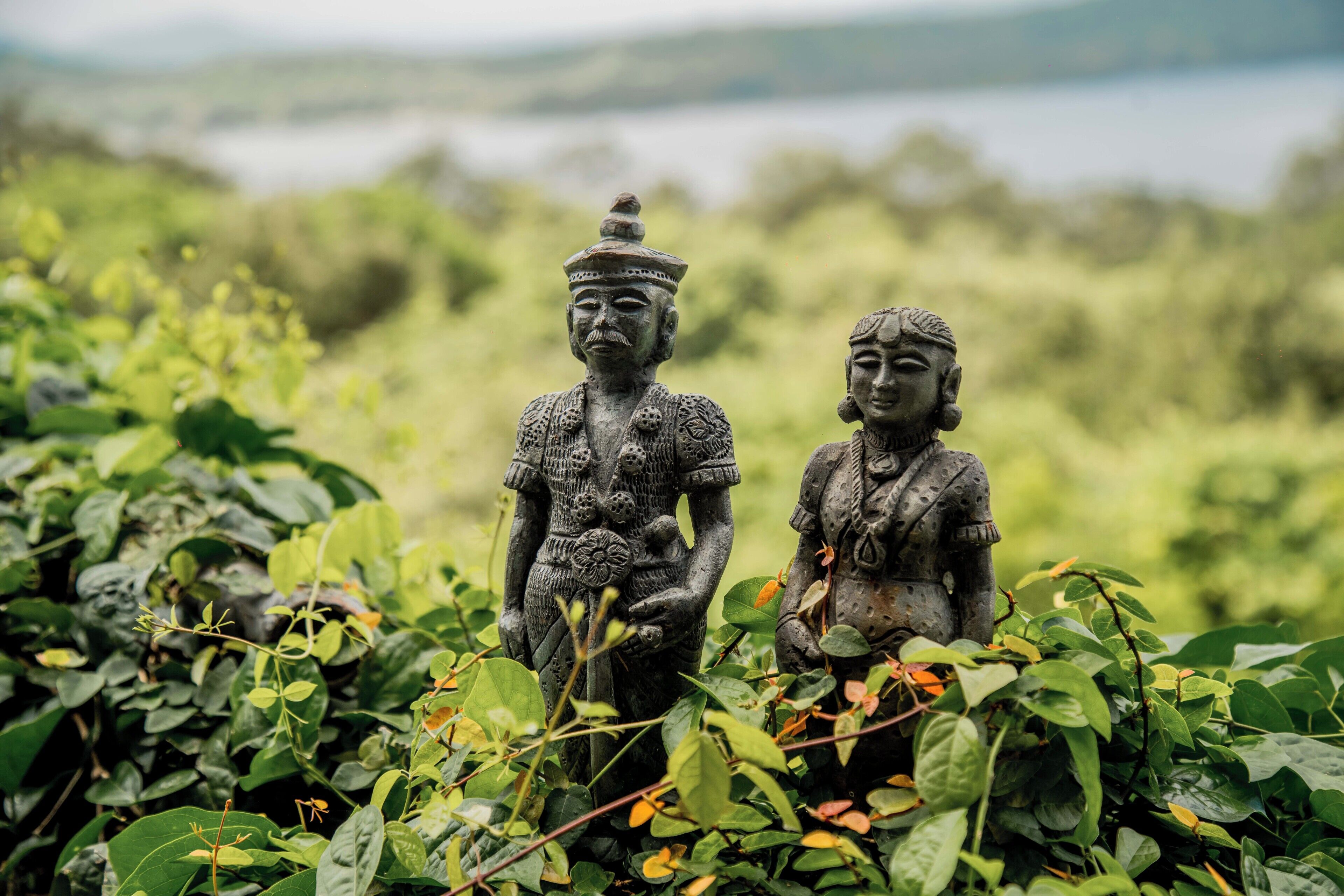 Two stone statues in a natural setting with greenery and a blurred background.