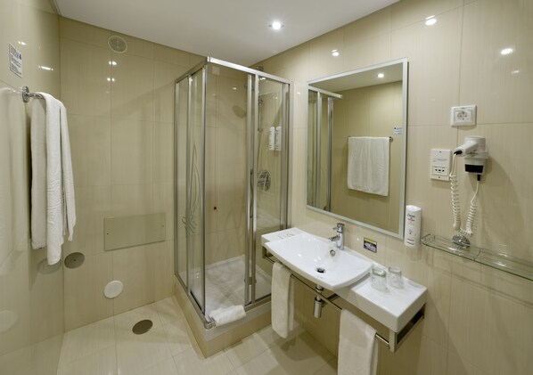 Un baño moderno con ducha de vidrio, lavamanos con espejo y secador de pelo en la pared.