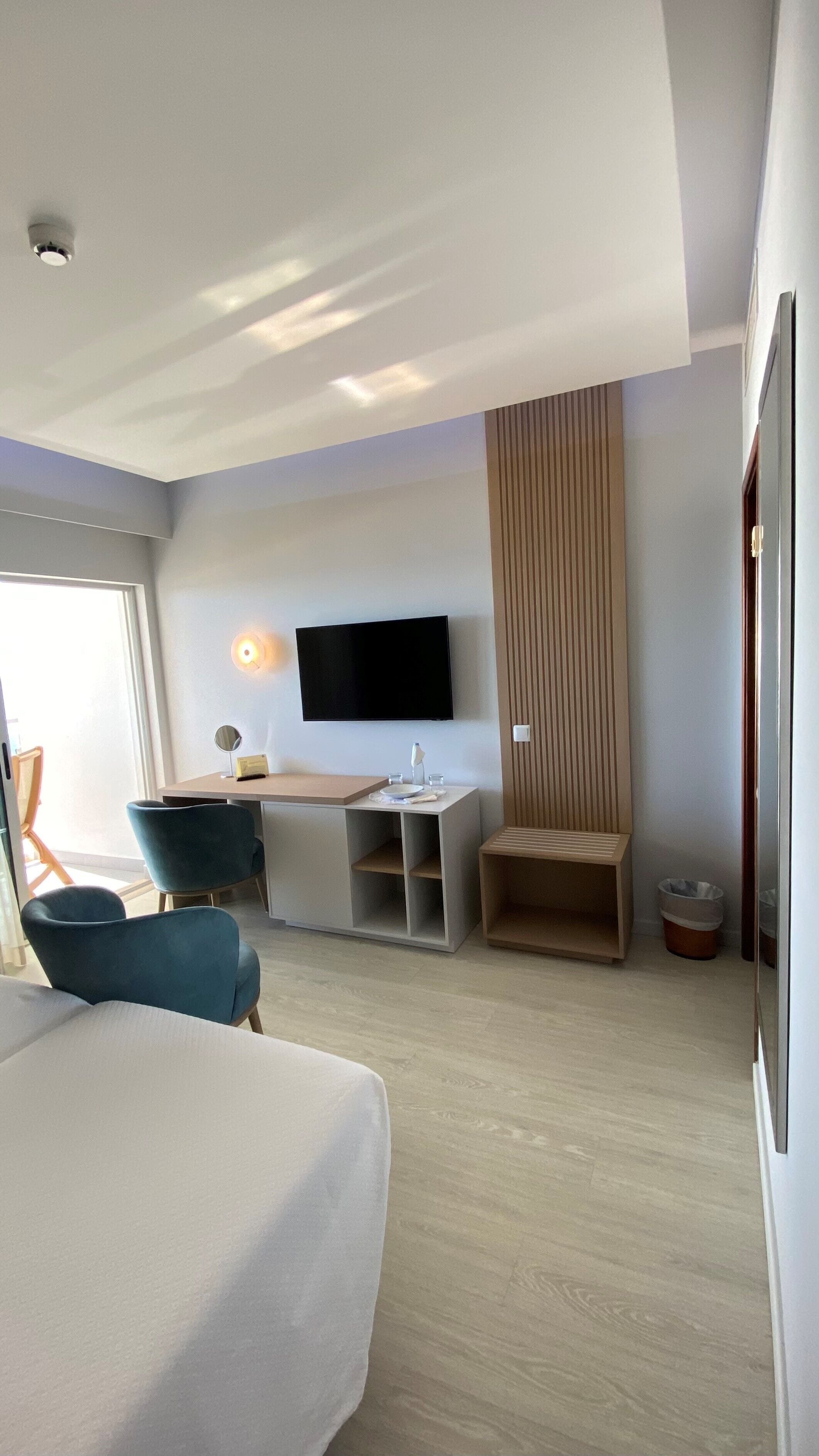 Et moderne hotelværelse med seng, skrivebord, stol, fjernsyn og et stort vindue.