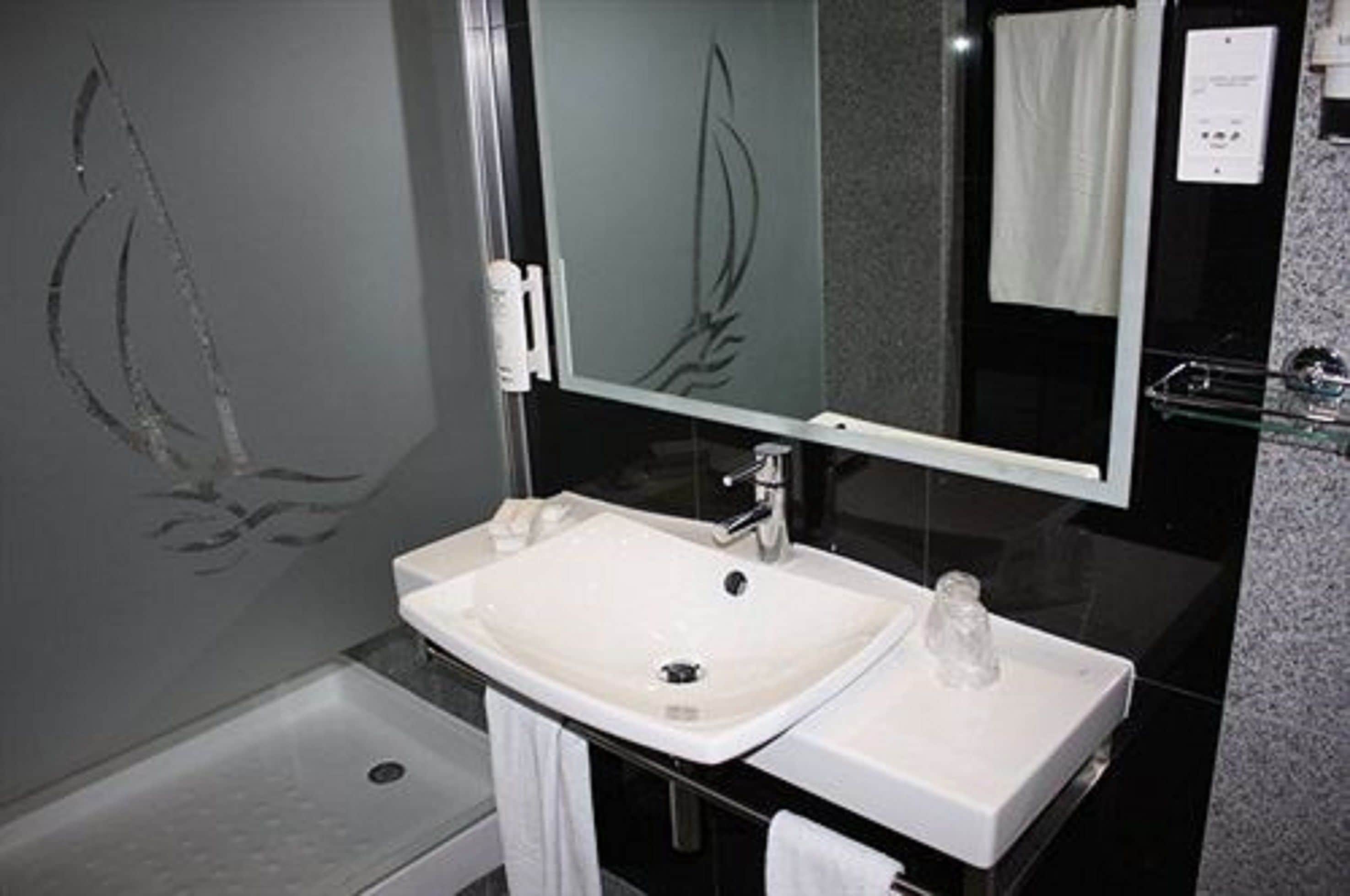 A modern bathroom with a white sink, a glass shower enclosure, and a large mirror.