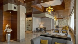 Un moderno vestíbulo de hotel con un sofá gris, una zona de comedor y un jarrón decorativo con flores.