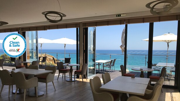Un restaurante con terraza al aire libre con vistas al mar, con sillas y mesas de mimbre, y una vista del océano.