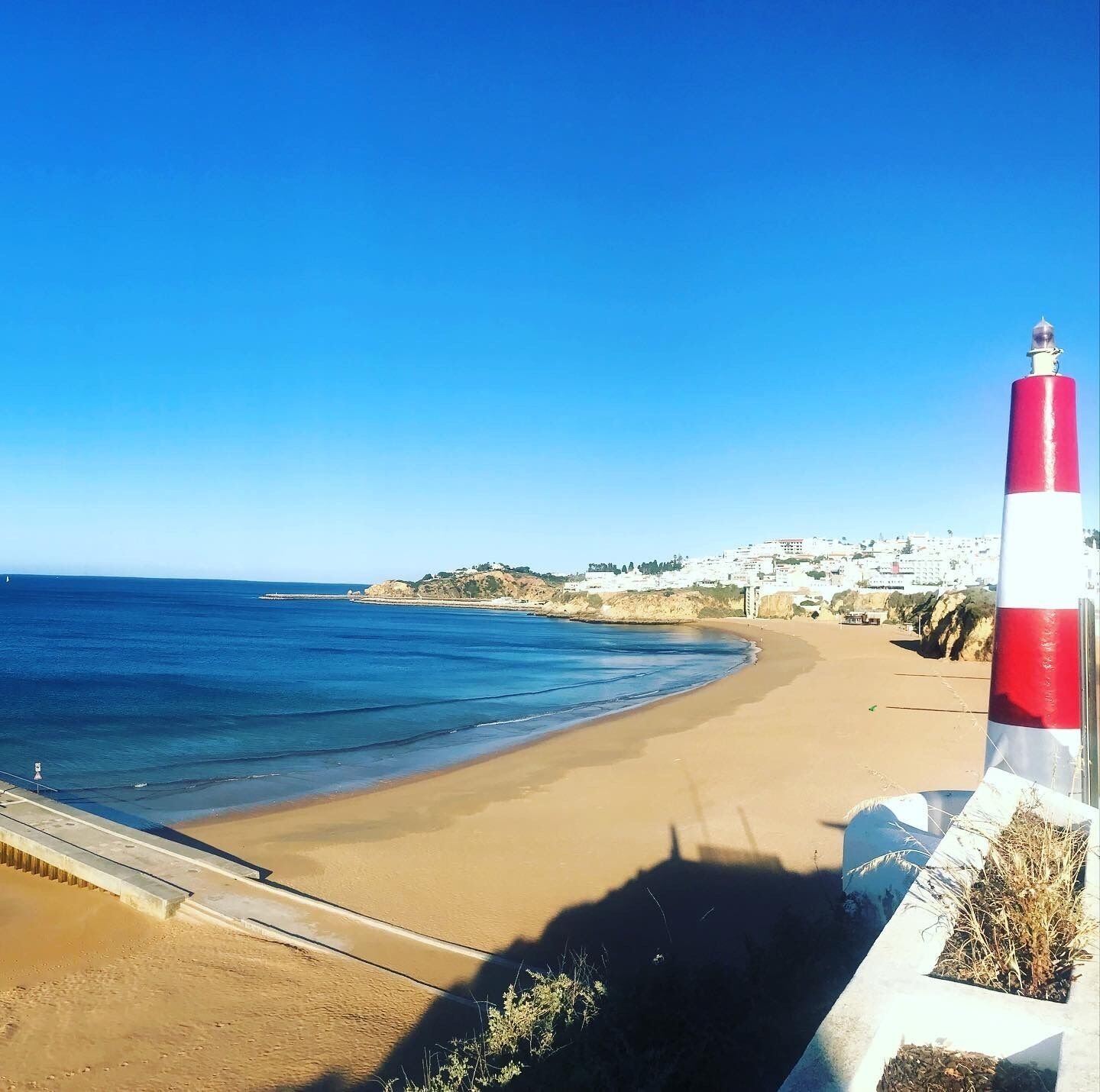 A coastal scene with a red and white lighthouse, sandy beach, and a town in the background.