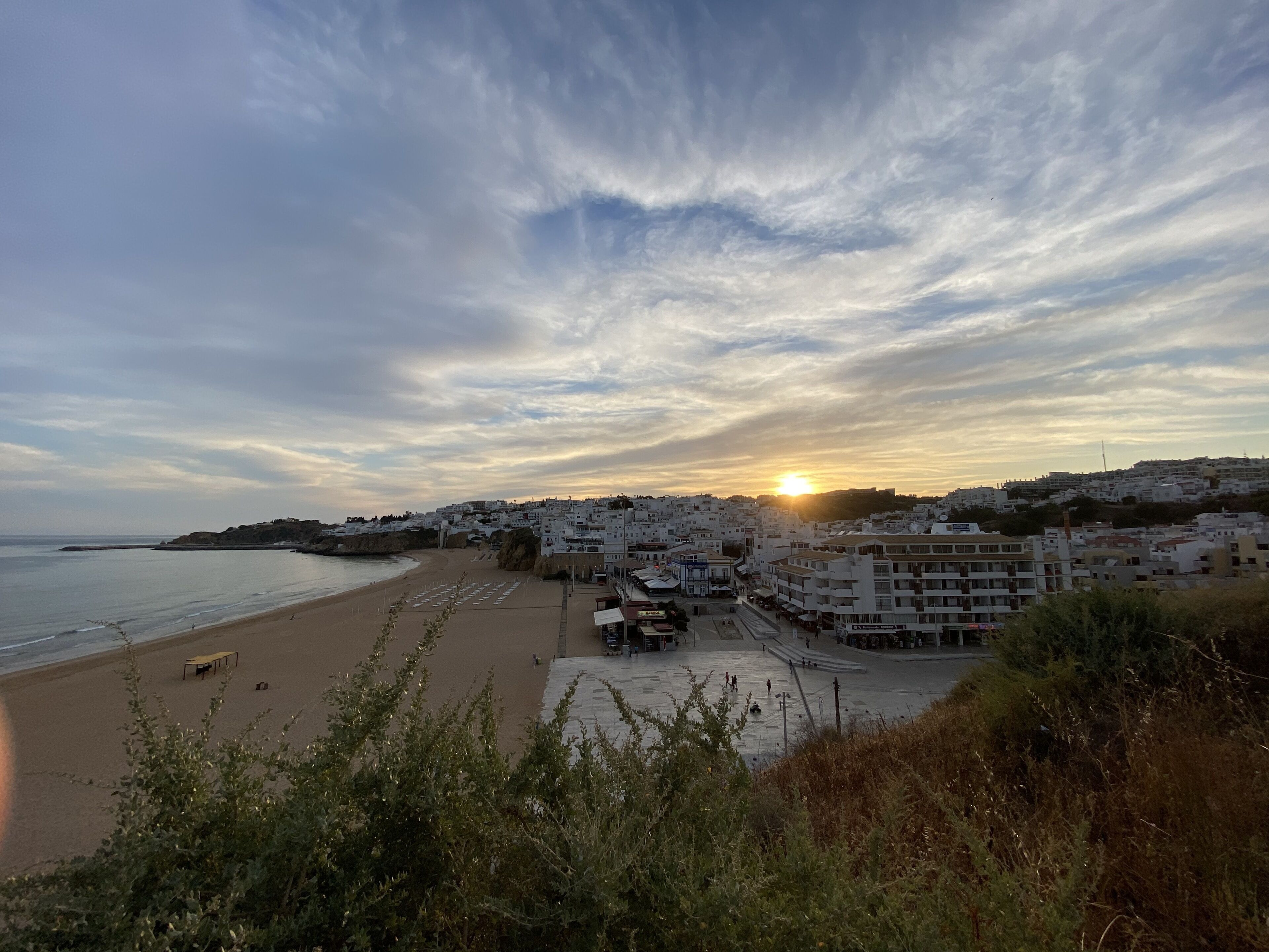 Eine Küstenstadt mit Strand, Gebäuden und einem Sonnenuntergang.