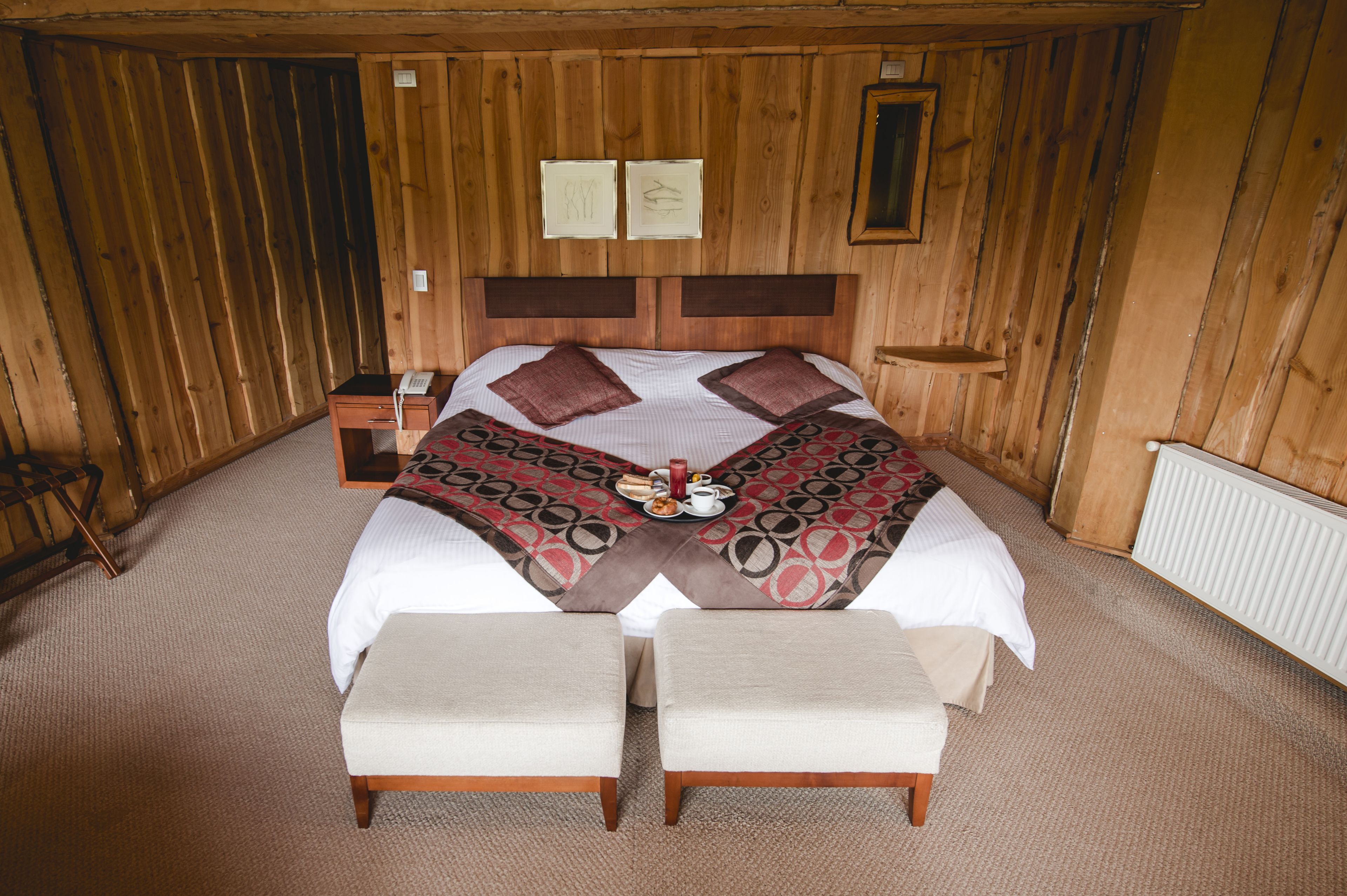 A wooden-paneled room with a bed, two bedside tables, and a small desk.