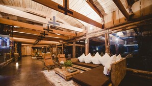 Un interior acogedor y rústico con vigas de madera, un sofá con cojines y un amplio ventanal con vistas al exterior.