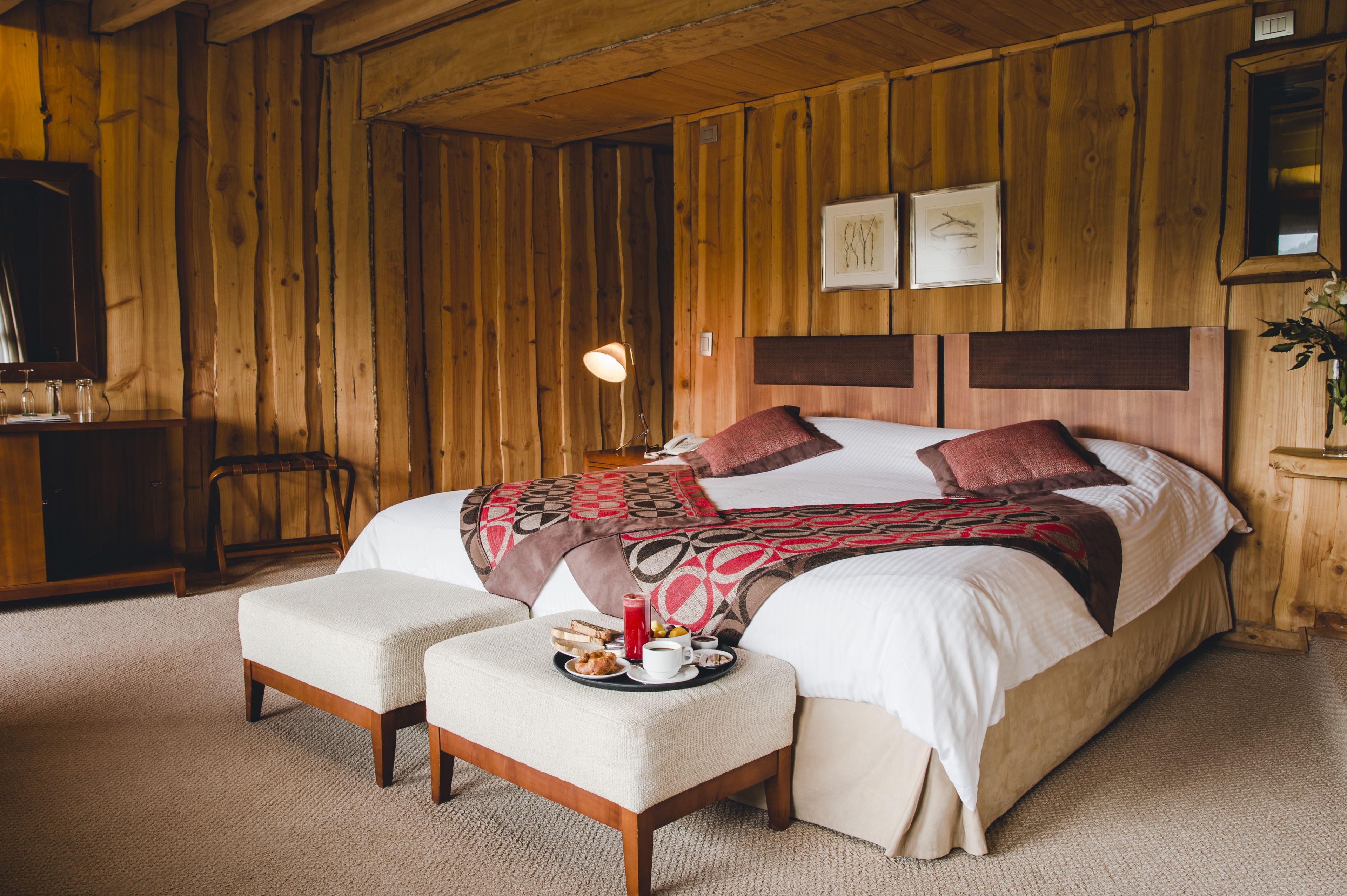 A wooden-paneled room with a bed, a bedside table, and a tray with breakfast items.