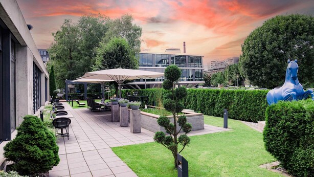 A modern outdoor patio area with a seating arrangement, a large blue sculpture, and a view of a building in the background. - Hotel Der Blaue Reiter Design- & Tagungshotel (Karlsruhe)