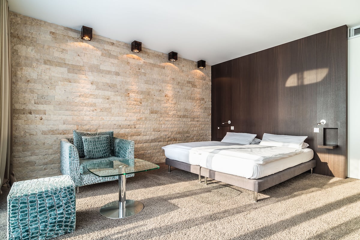 Un dormitorio moderno con pared de ladrillo, panel de madera, una mesa de centro de vidrio, un sofá y una cama.