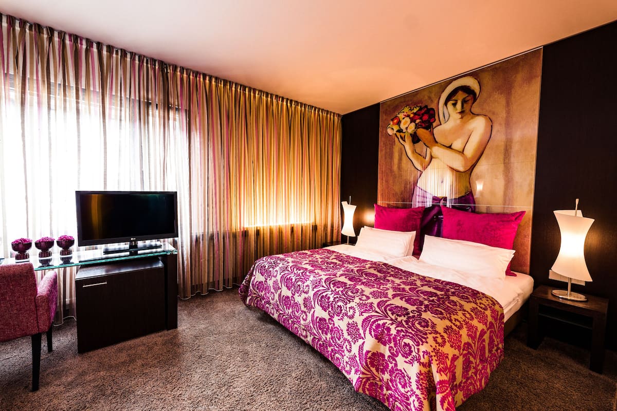 Una habitación de hotel con una cama, televisor, escritorio y un cuadro grande en la pared.