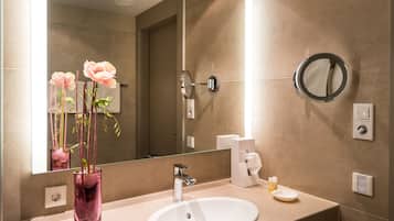 Un baño con un espejo grande, un lavamanos, dispensador de toallas y un florero con flores.