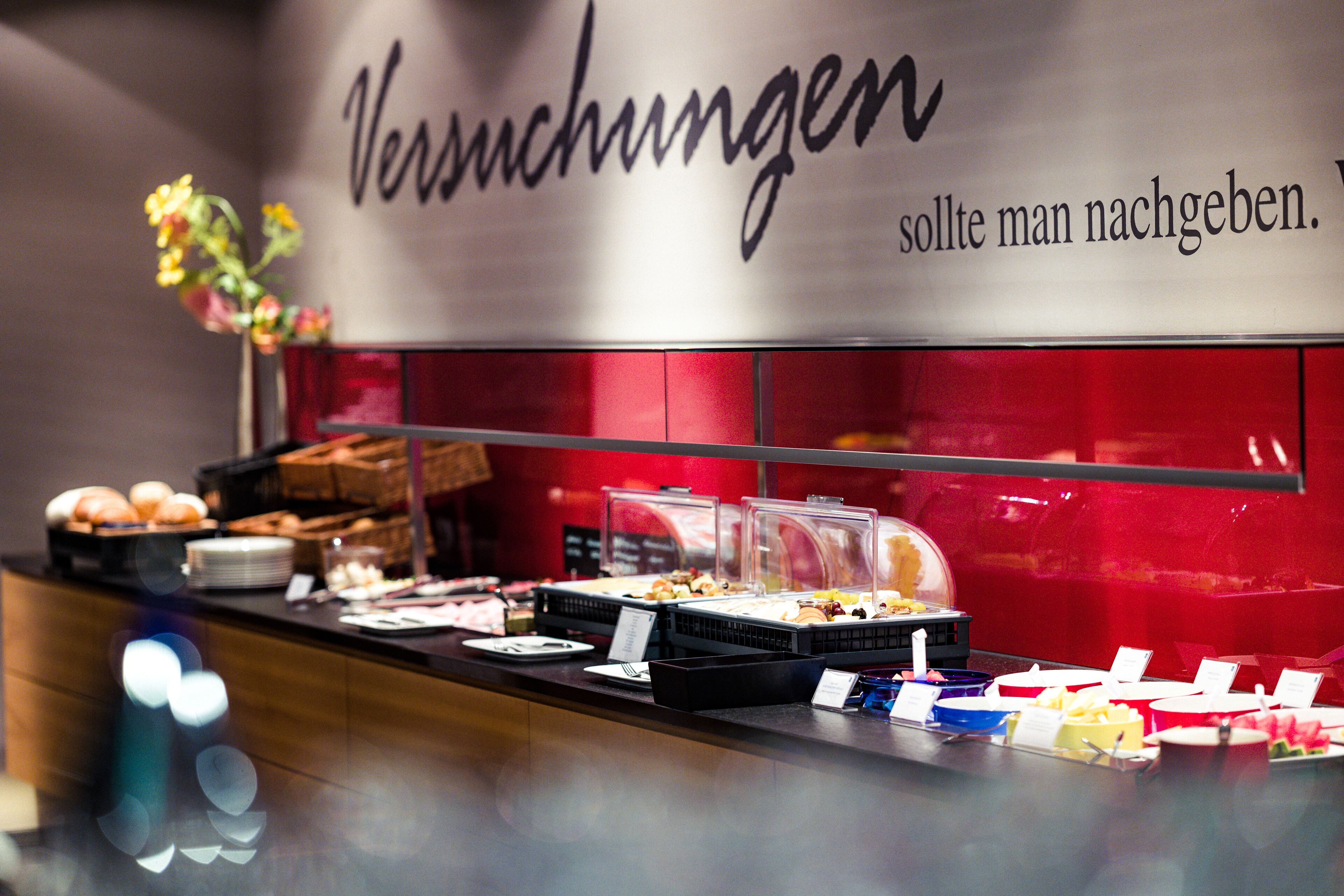 A buffet area with various food items and a sign that reads "Versuchungen" and "should man nachgeben."