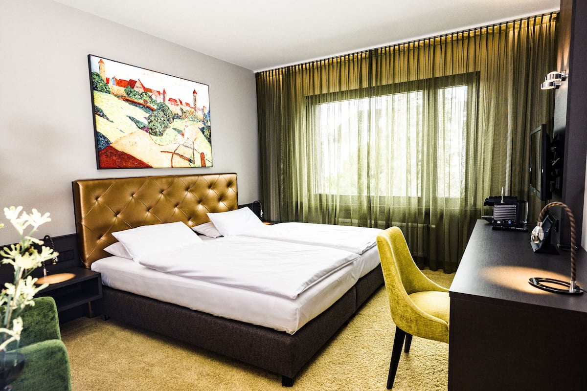 Habitación de hotel con una cama grande, un escritorio con silla, un cuadro en la pared y una ventana con cortinas.