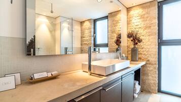 Un baño moderno con un espejo grande, un lavabo blanco y una pared decorativa de piedra.