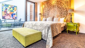A modern hotel room with a large bed, a green nightstand, a decorative headboard, a colorful abstract painting, and a view of the city through large windows. - Hotel Der Blaue Reiter Design- & Tagungshotel (Karlsruhe)