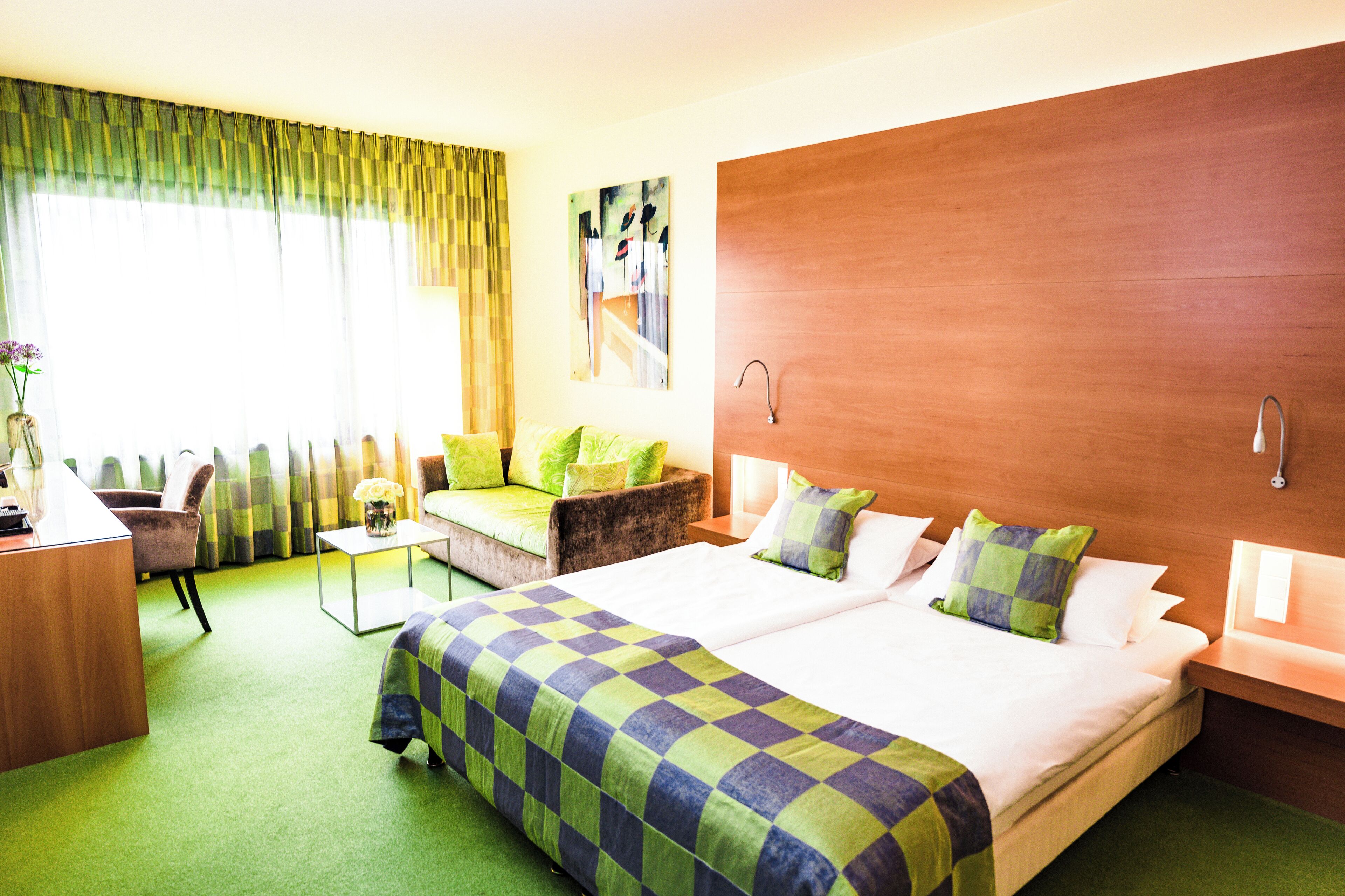 Ein Hotelzimmer mit einem großen Bett, einem Schreibtisch, einem Sessel und einem kleinen Tisch mit einer Blumenvase.