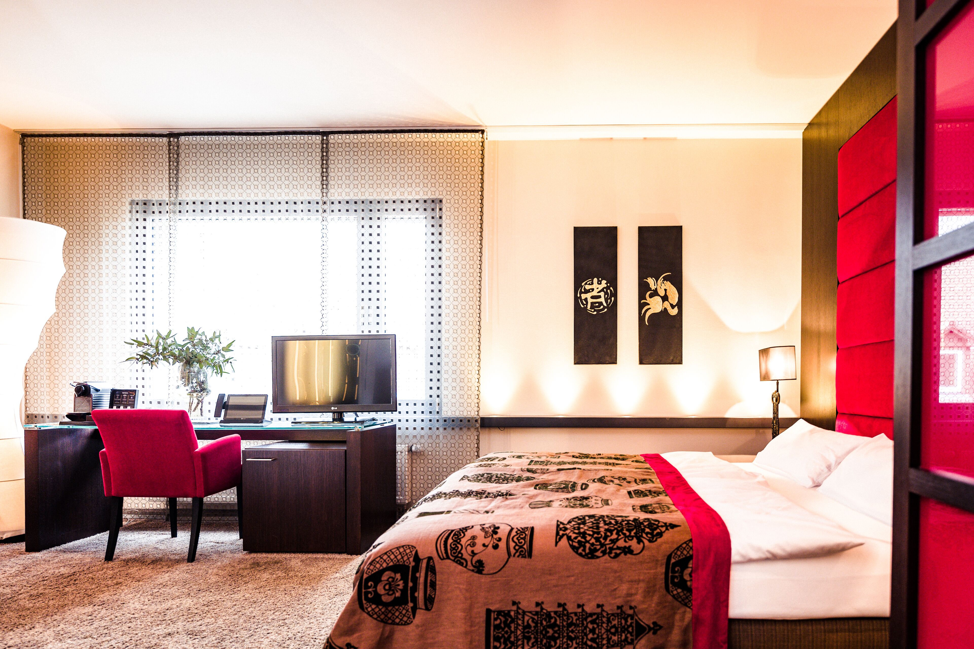 Habitación de hotel con cama, escritorio y silla. Hay un televisor en el escritorio y una planta en la esquina.