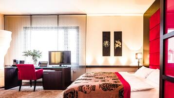 Habitación de hotel con cama, escritorio y silla. Hay un televisor en el escritorio y una planta en la esquina.