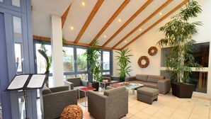 A spacious lobby with multiple seating areas, large windows, and potted plants.