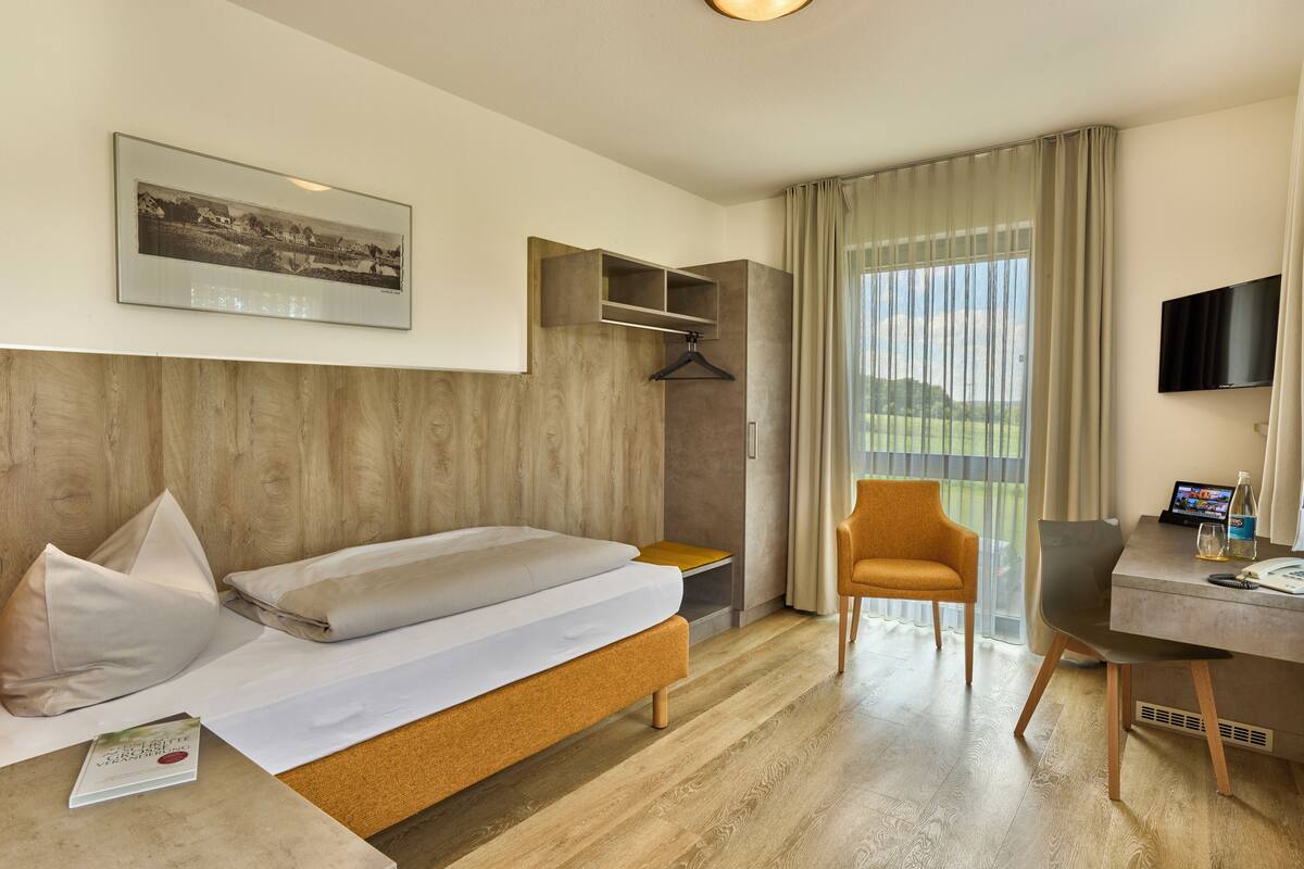 A hotel room with a bed, a desk, a chair, a TV, and a window with curtains.