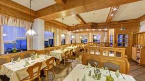 Restaurante com interiores de madeira, várias mesas de jantar e vista para o mar através de grandes janelas.