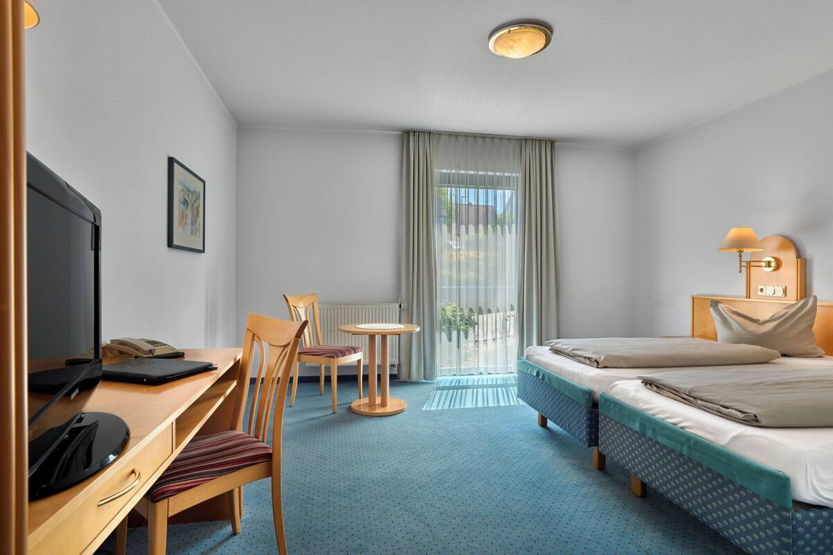A hotel room with a bed, desk, chair, and a TV.