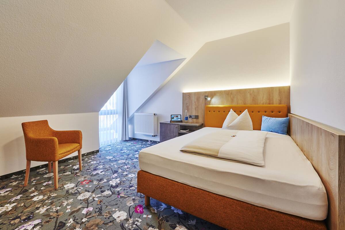 A modern hotel room with a large bed, a wooden headboard, a desk, and a chair.
