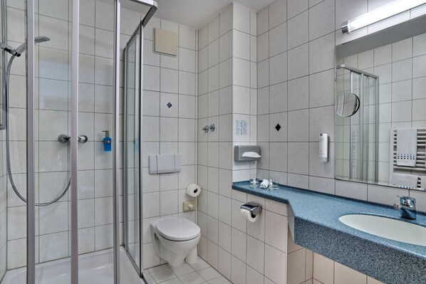 A modern bathroom with a glass shower enclosure, a toilet, a sink with a blue countertop, and a mirror above the sink. - Landhotel Seerose (Langenzenn)
