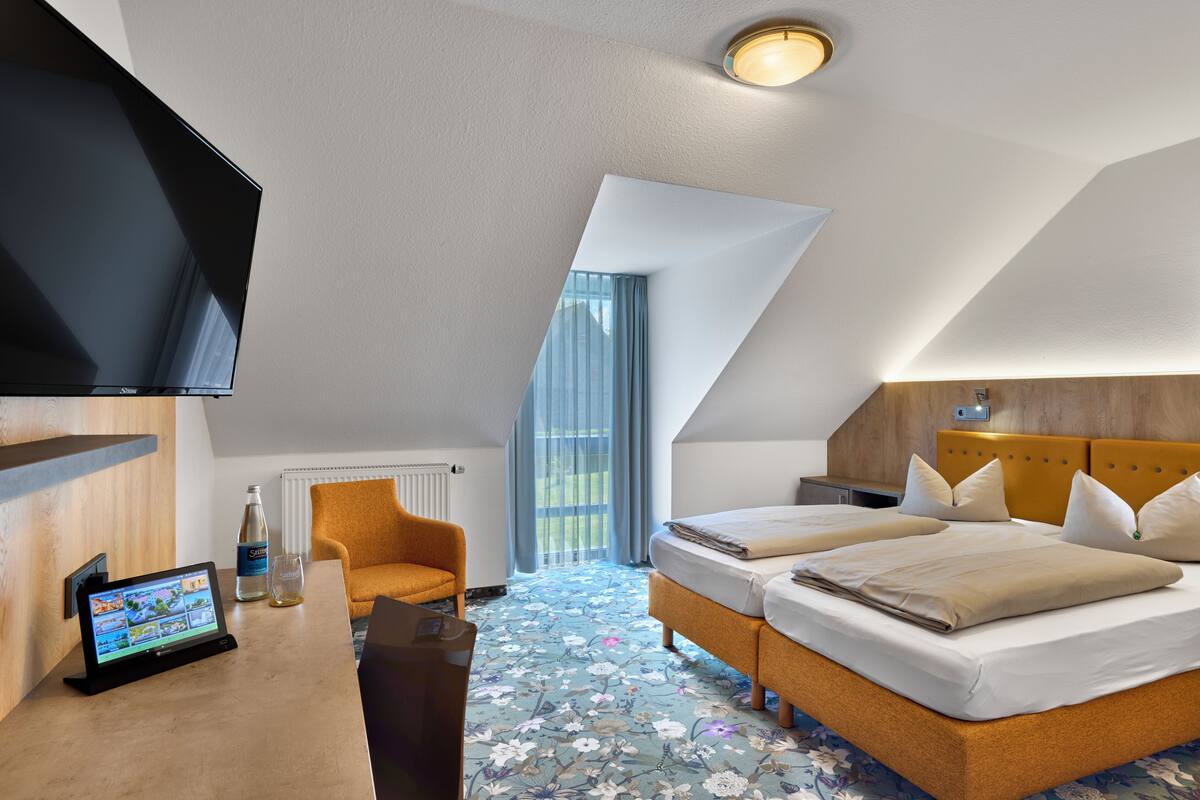 A modern hotel room with a large bed, a flat-screen TV, a desk with a computer, and a window with curtains.