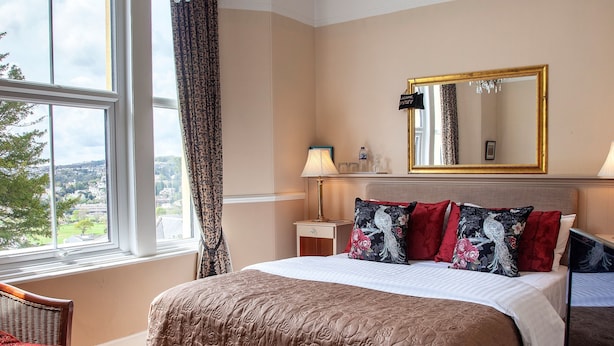A hotel room with a large bed, a nightstand, a lamp, a mirror, and a view of the outside. - Court Prior Boutique B&B and Apartment (Torquay)