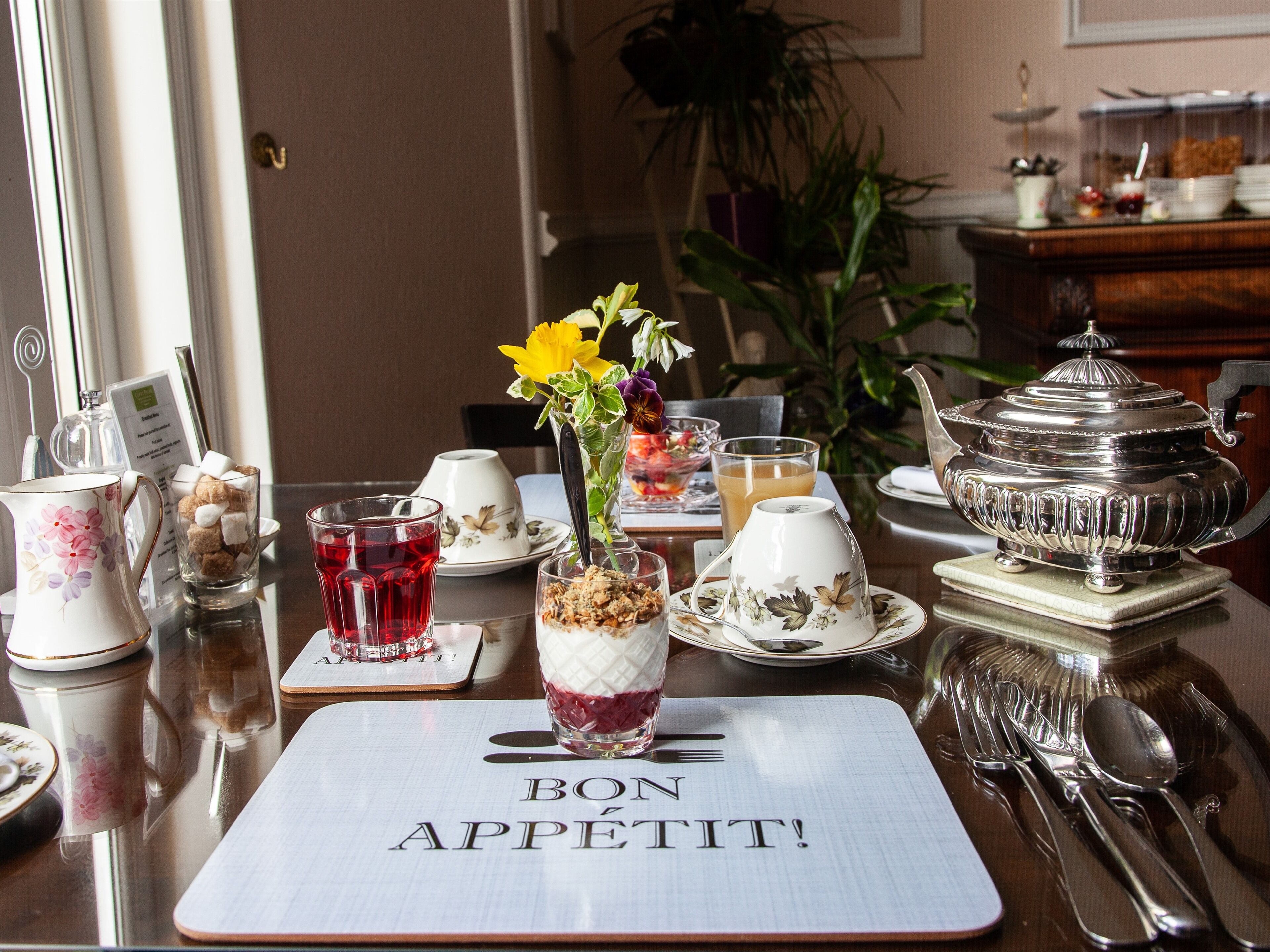 A dining table set with a variety of tableware, including a pitcher, teacups, a sugar bowl, and a silver teapot.