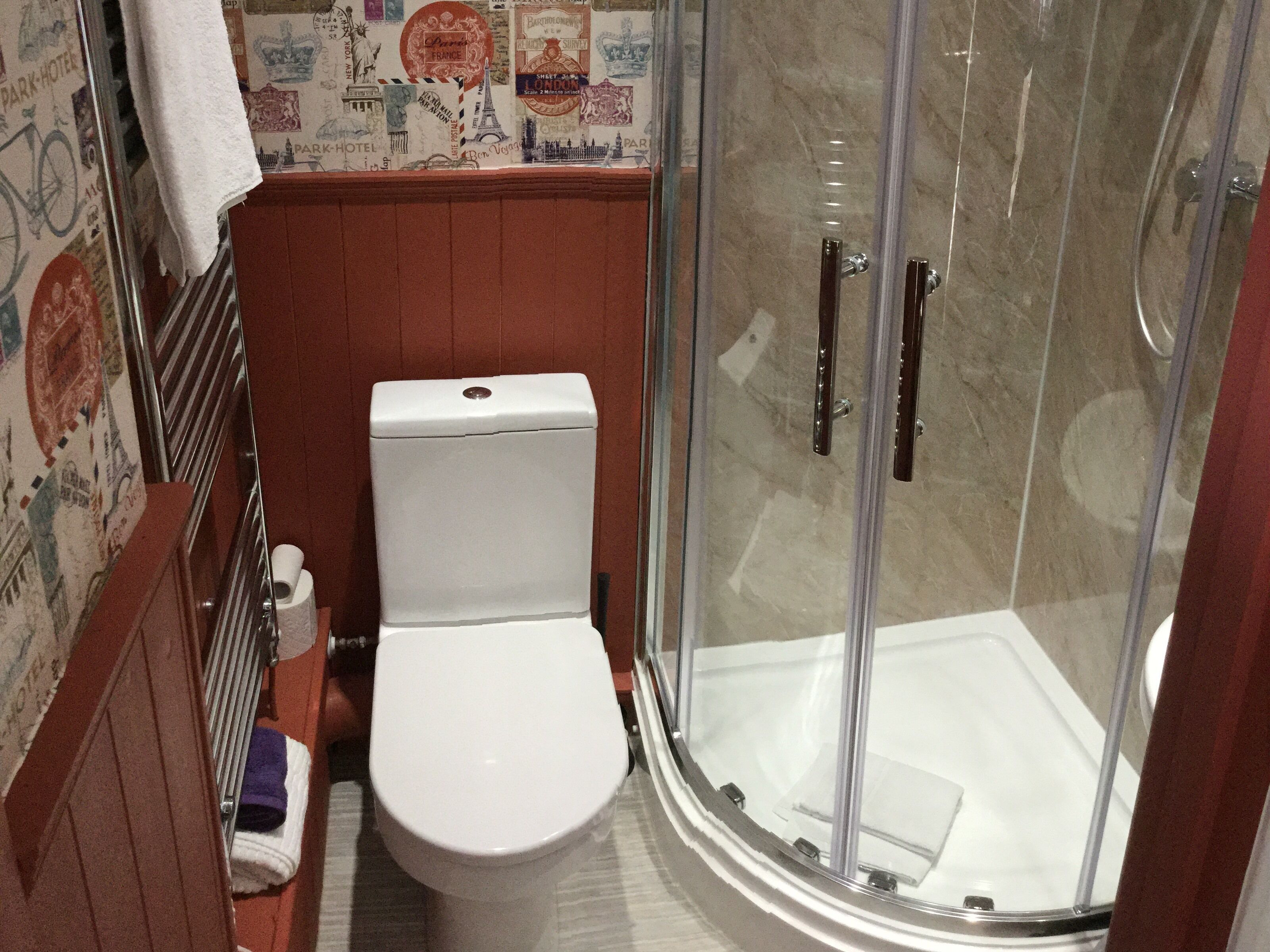 Un bagno con un water bianco, cabina doccia in vetro e una parete decorata con elementi a tema viaggio.