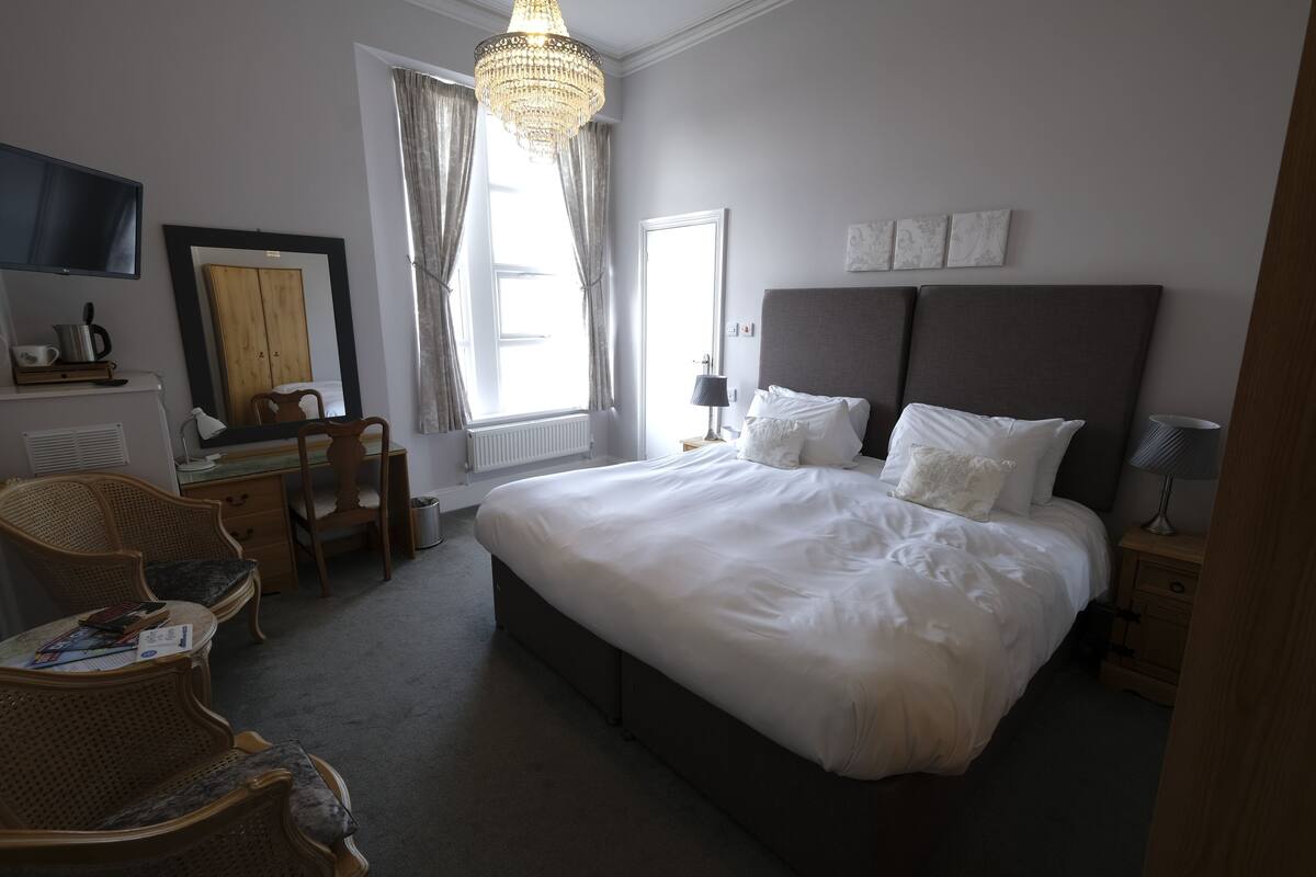 A bedroom with a large bed, a desk, a chair, and a television on the wall.