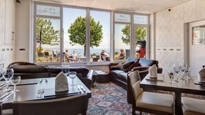 Un restaurante con vistas al mar, que ofrece un rincón de estar acogedor con sofás y mesas para comer.