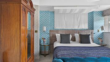 Une chambre avec une grande armoire en bois, un lit avec une literie à motifs et une tête de lit recouverte de tissu bleu.