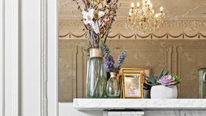 A room with a marble fireplace, a green velvet chair, a chandelier, and a shelf with decorative items. - The Torcroft (Torquay)