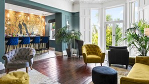 A spacious living area with a bar, comfortable seating, and large windows offering a view of greenery. - The Torcroft (Torquay)
