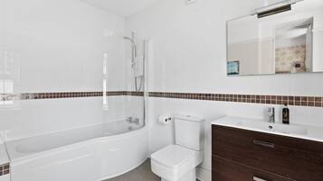 A modern bathroom with a bathtub, toilet, and vanity with a mirror.