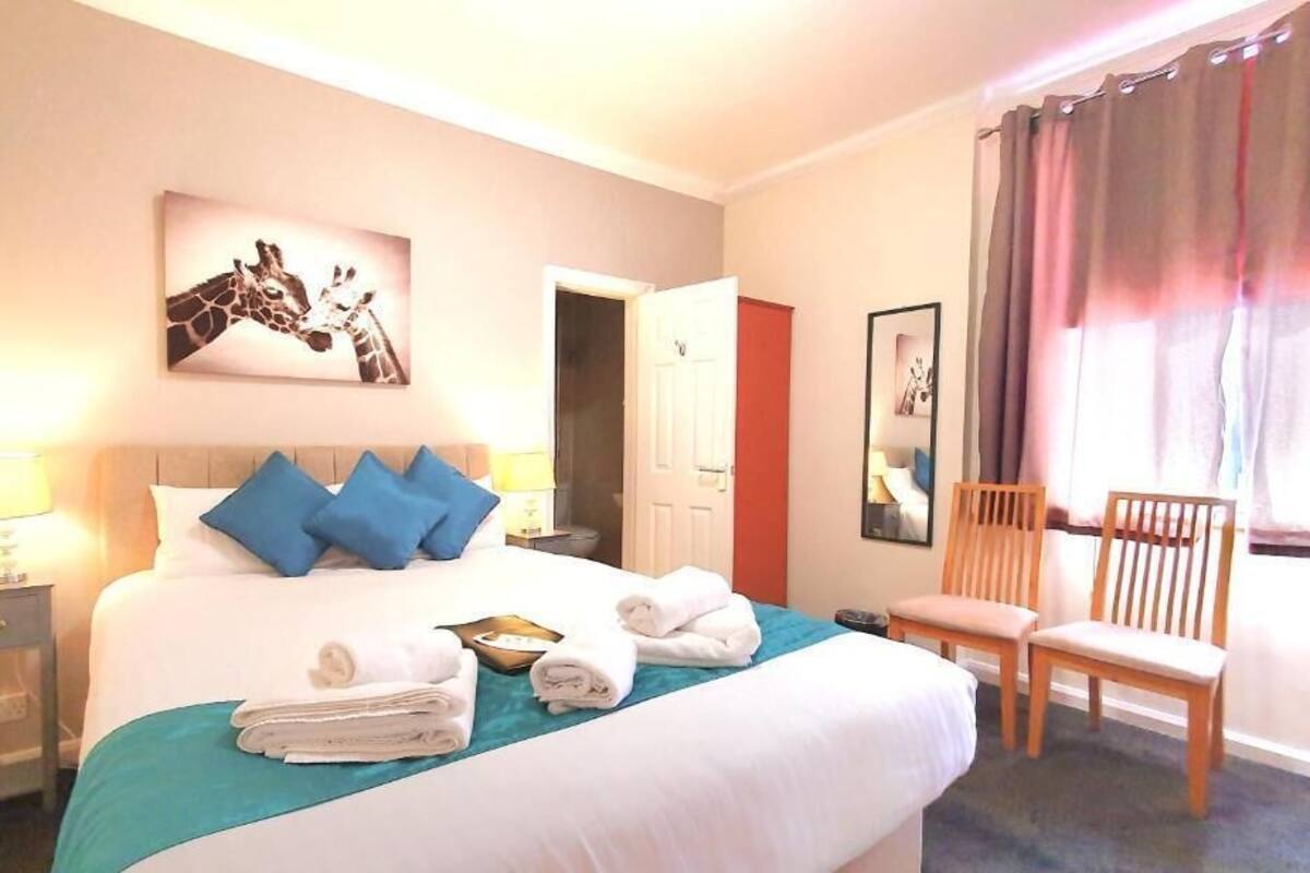 A hotel room with a bed, pillows, a chair, a nightstand, and a painting on the wall.