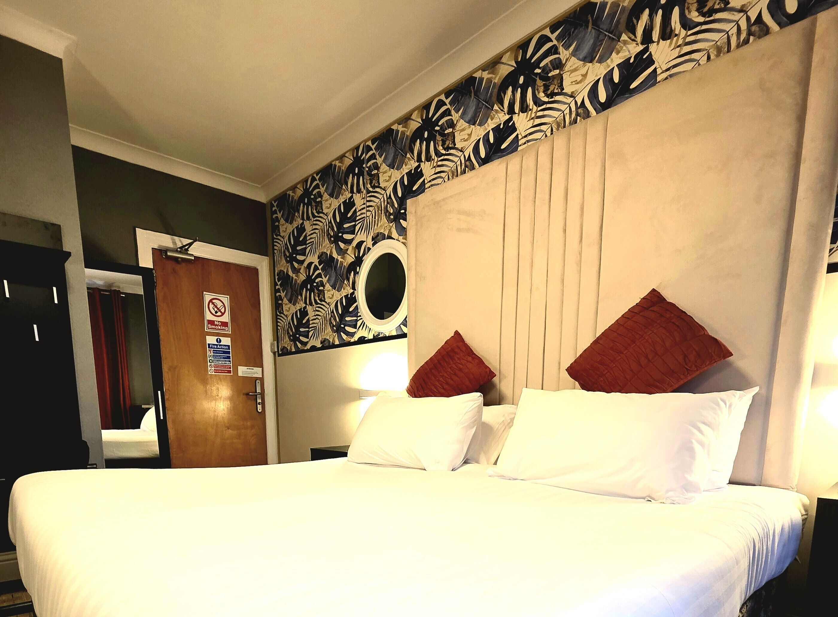 Una camera d'hotel con un letto grande, una testiera con uno specchio circolare e una parete decorata con motivi floreali.