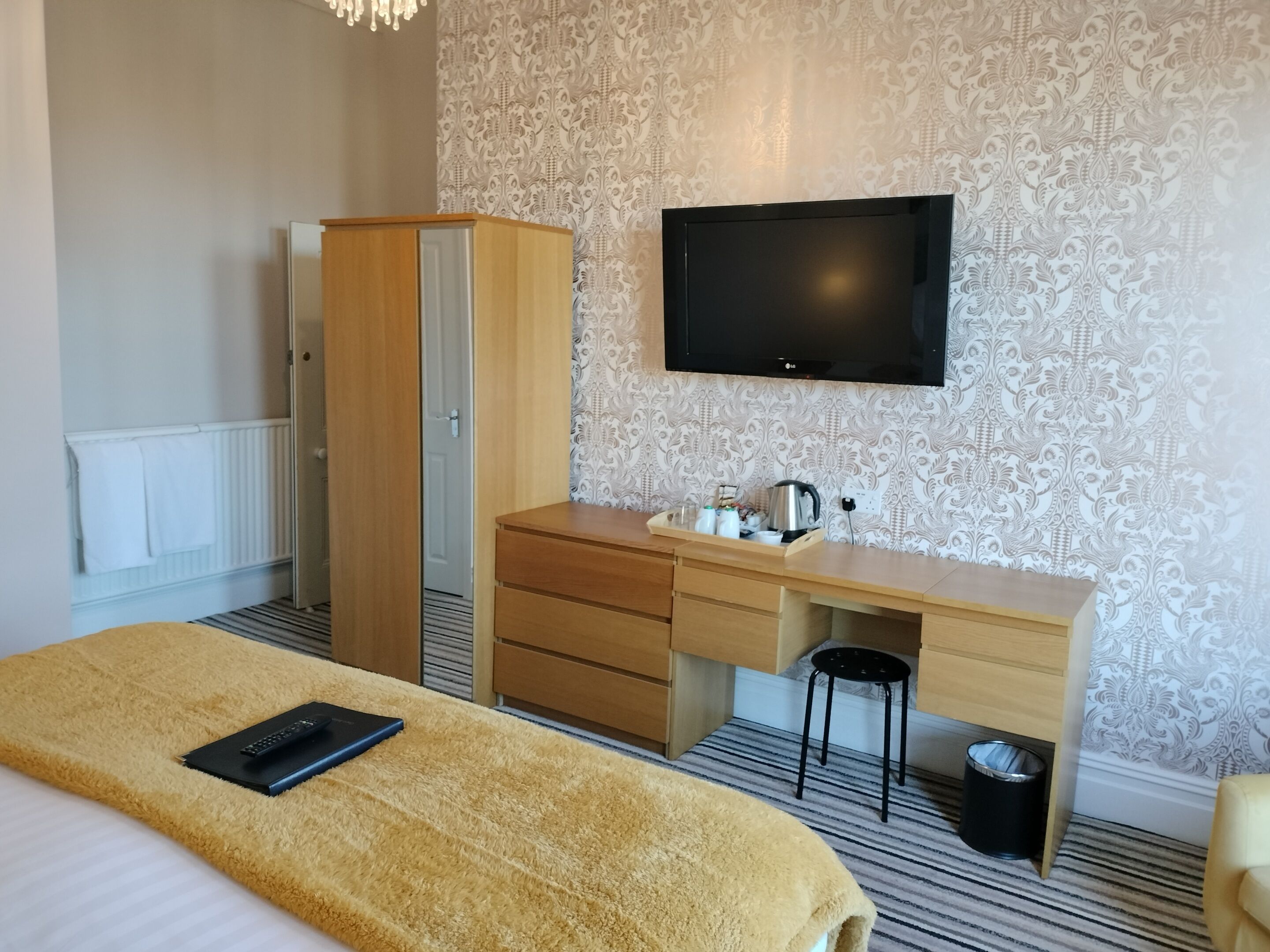 Una habitación de hotel con una cama, un escritorio de madera, un televisor y un armario.