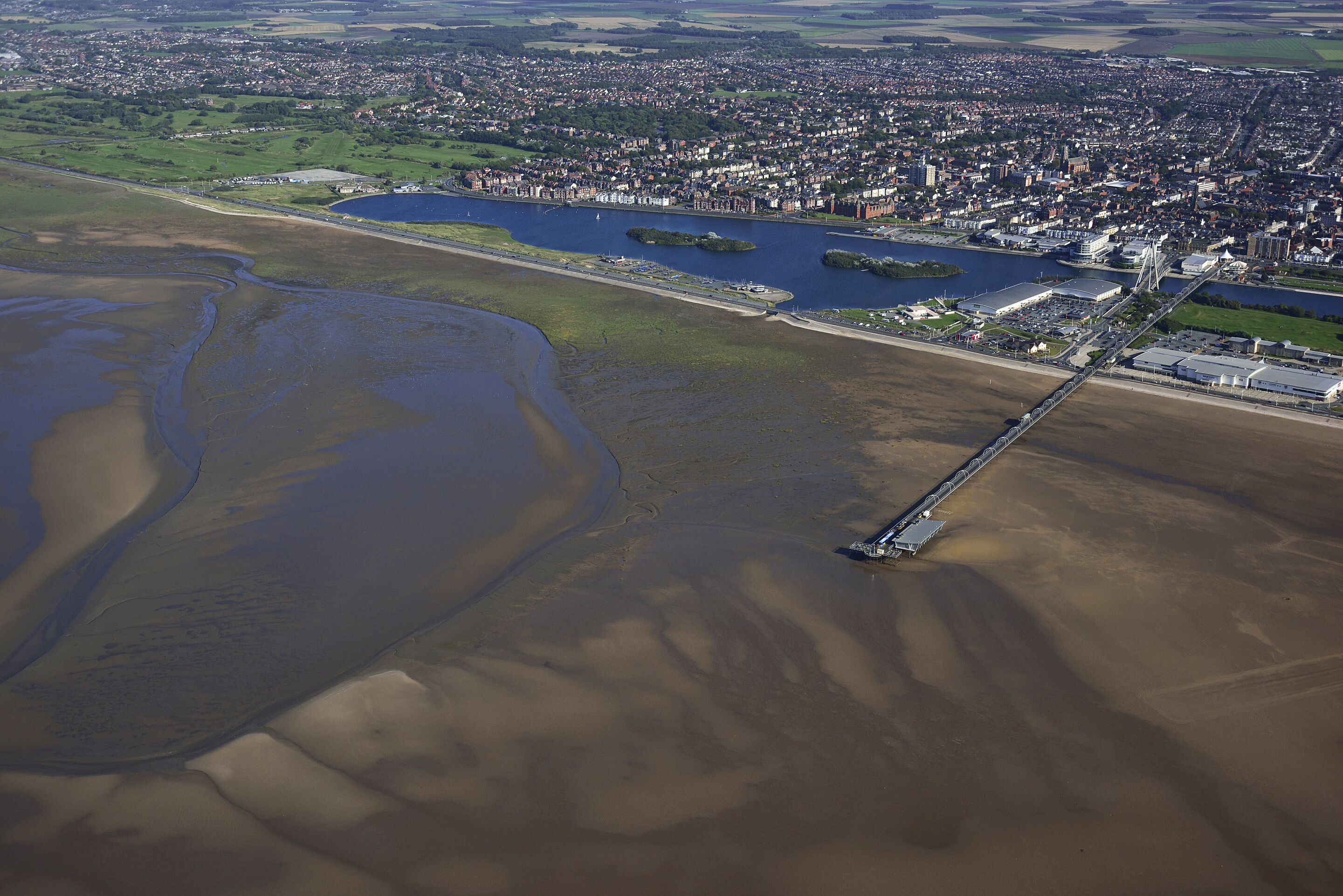 Luftaufnahme einer Küstenstadt mit Fluss, Brücke und weitem Wasserareal.
