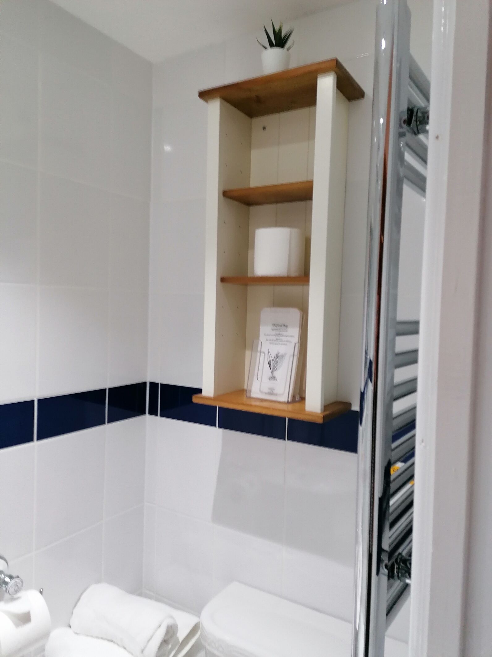Un baño con azulejos blancos, un estante de madera con un cuadro enmarcado y una franja azul en la pared.