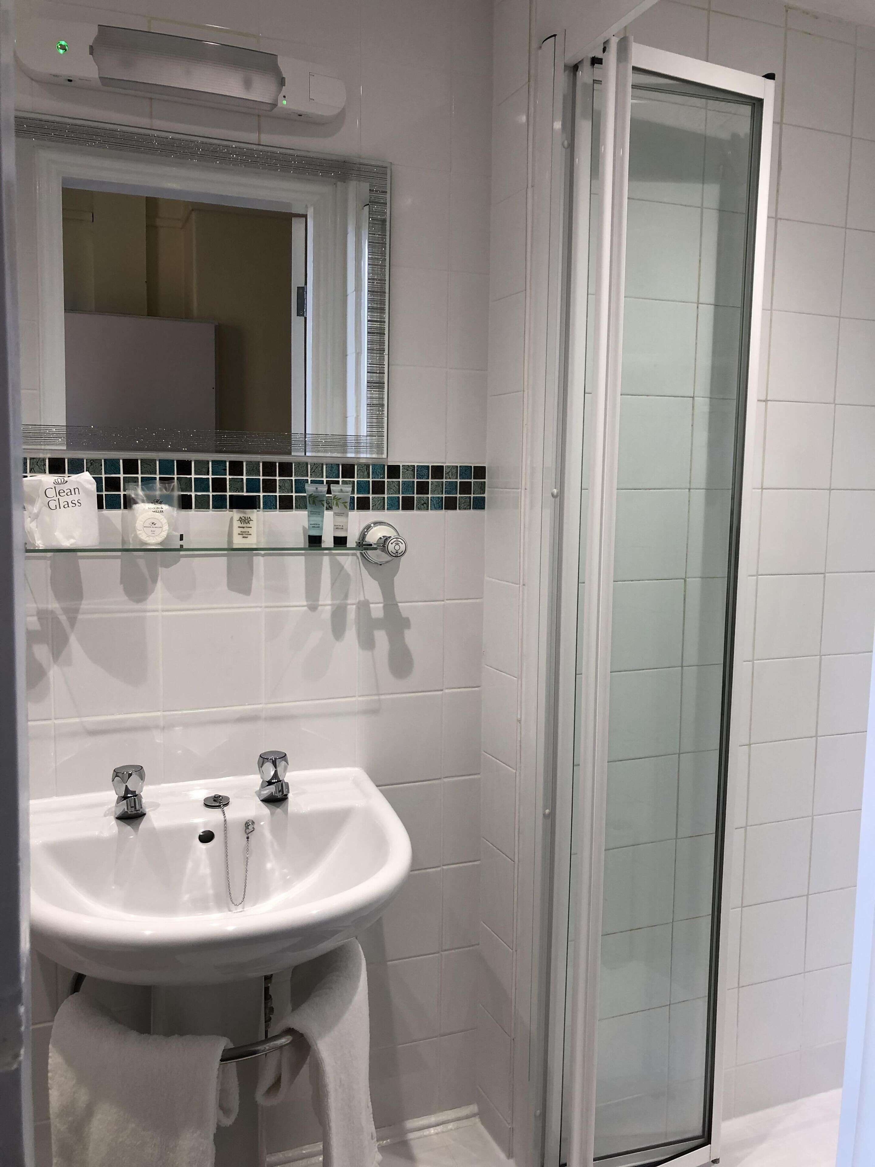 Un bagno con un lavandino bianco, uno sportello doccia in vetro e uno schienale piastrellato.